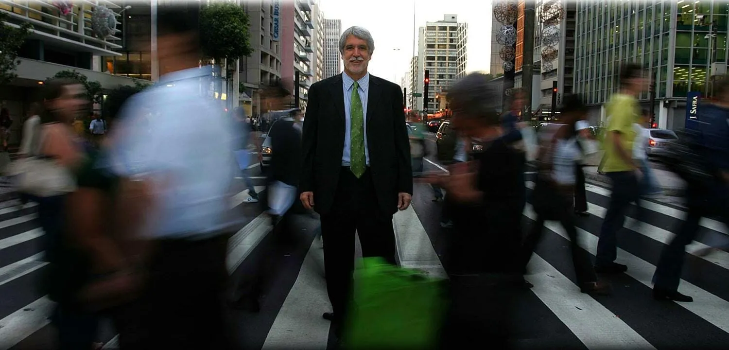 Enrique Peñalosa standing still on a busy pedestrian crossing while people hurry past him