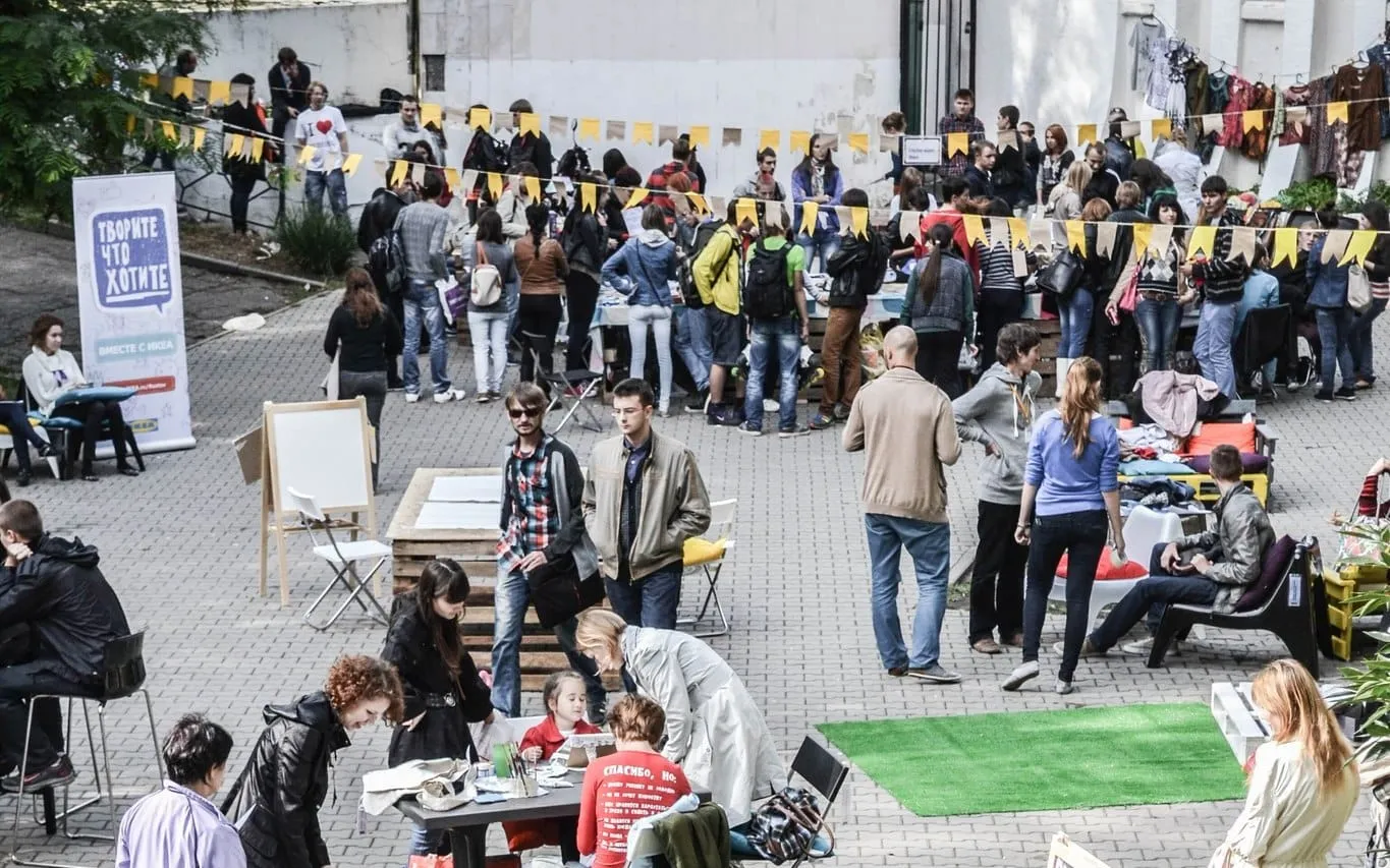 A crowded festival courtyard with yellow bunting, tables and people talking