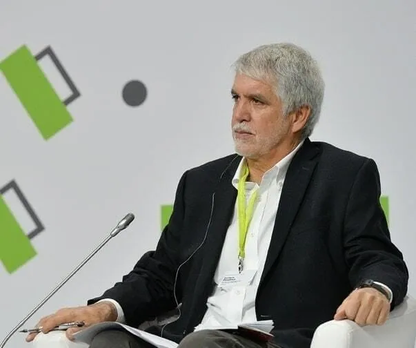 Enrique Peñalosa in an armchair on a conference stage, with a microphone in front of him