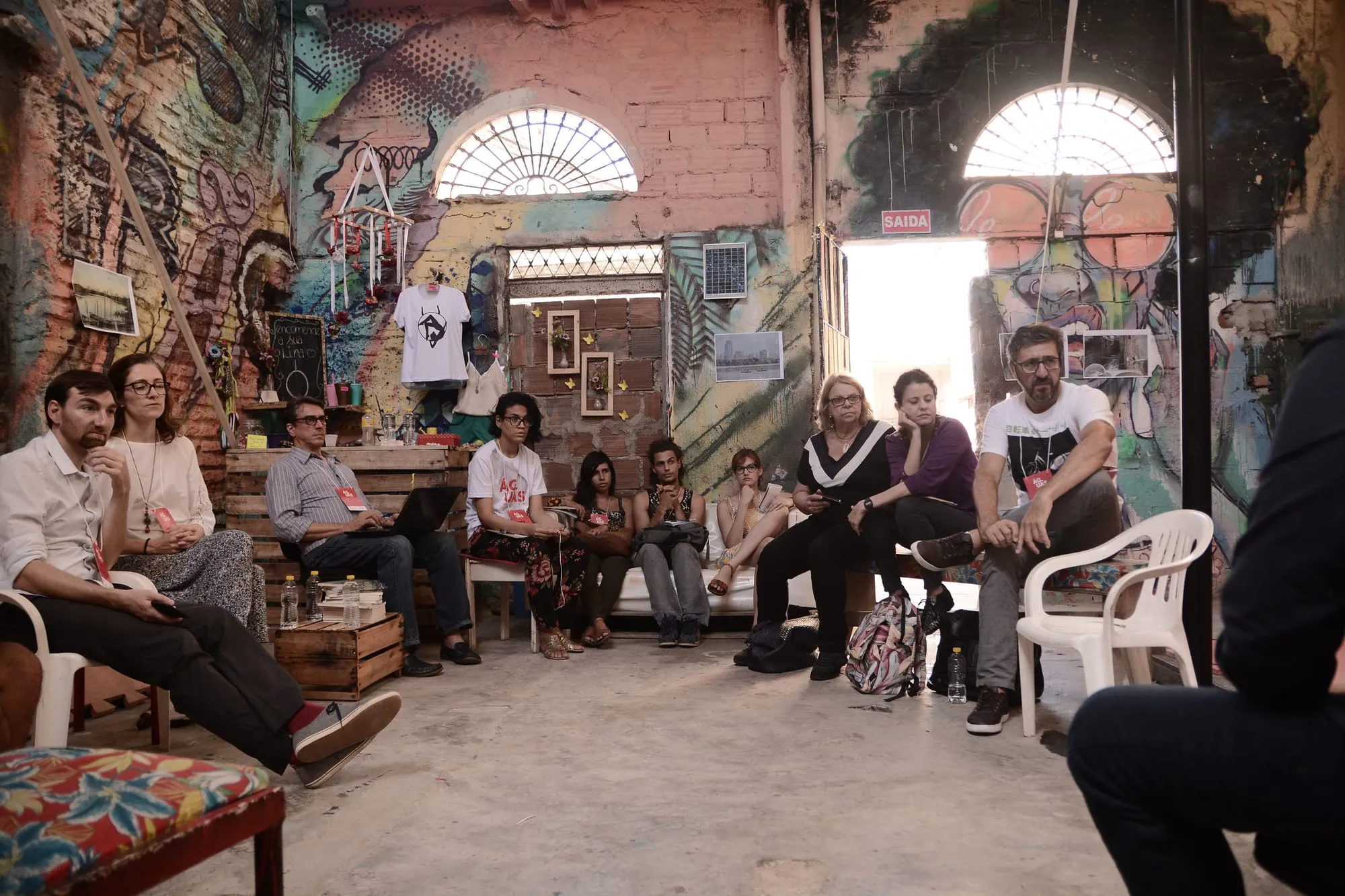 Participants sitting in a circle in a brick hall with colourful murals in Recife