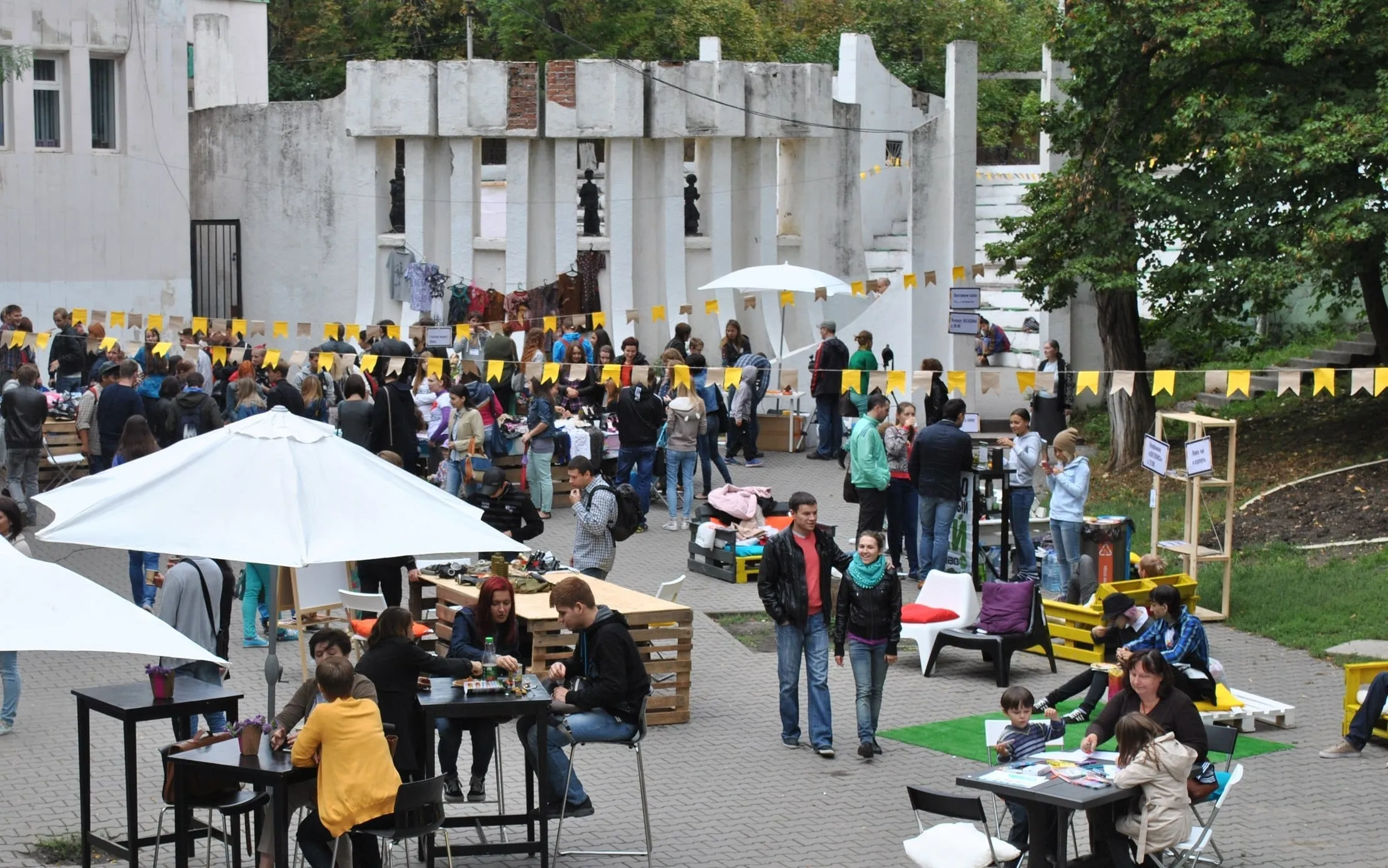 Urban Festival Rostov: people at tables and pallet furniture under yellow flags in a courtyard amphitheatre